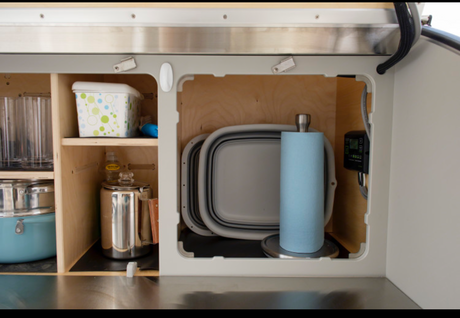 RV rental: Organized compact kitchen space with cookware, glasses, paper towels, & collapsible dishes.
