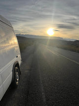 White RV rental van parked roadside, sun setting over distant mountains. Scenic road trip vibes.