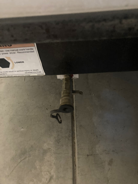An RV rental's manual crank port for lowering stabilizer jacks, including a warning label.