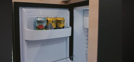 An open mini-fridge in an RV rental, stocked with three cans of Whistler Brewing Co. beer, ready for your road trip.