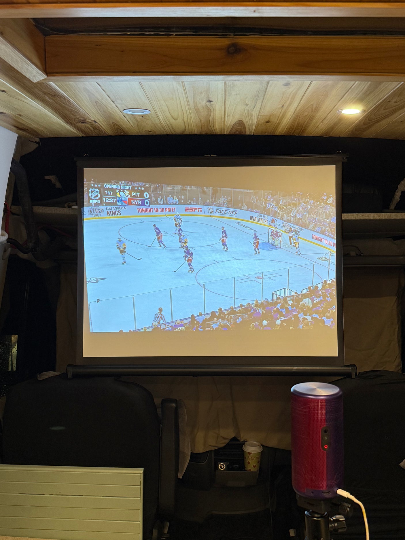 RV rental fun: A projector displays NHL hockey on a screen, offering cozy, on-the-go entertainment in a wood-paneled interior.