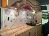 Experience this unique RV rental! Custom van interior featuring a vibrant kitchen with artistic decor, functional countertop, and cooking area.