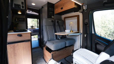 Inside this stylish rv rental: swivel seats, dining table, controls, kitchen unit, and a comfortable bed. Ready for travel.