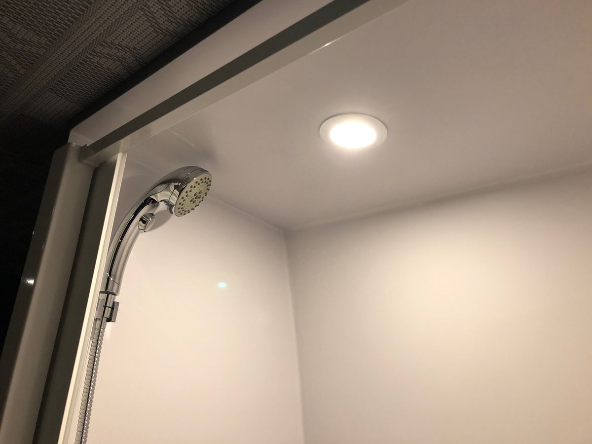 RV rental shower: Brightly lit, compact white interior with a chrome shower head and recessed ceiling light. — photo 10