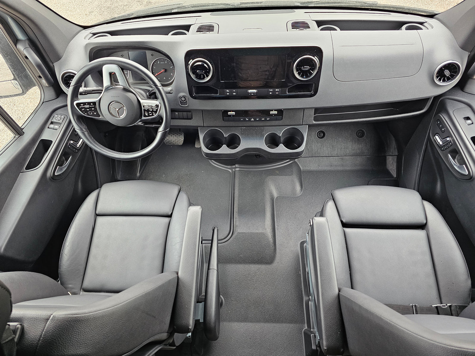 Modern rv rental van cockpit: dashboard, Mercedes steering wheel, infotainment, dual seats, and cup holders visible.