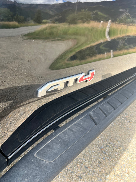 Shiny black GMC AT4 truck for RV rental, reflecting mountains & road. Includes running board for easy access.