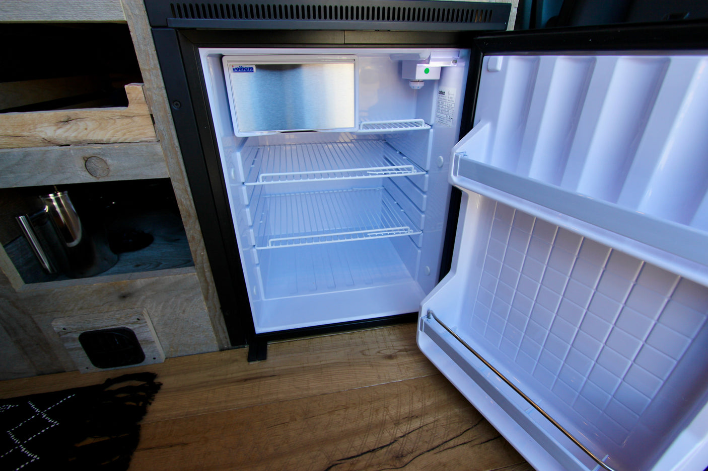 This open mini-fridge in an rv rental showcases its clean white interior, wire shelves, and small freezer.