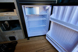 This open mini-fridge in an rv rental showcases its clean white interior, wire shelves, and small freezer.