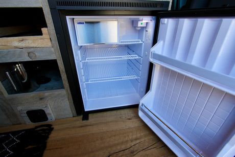 This open mini-fridge in an rv rental showcases its clean white interior, wire shelves, and small freezer.