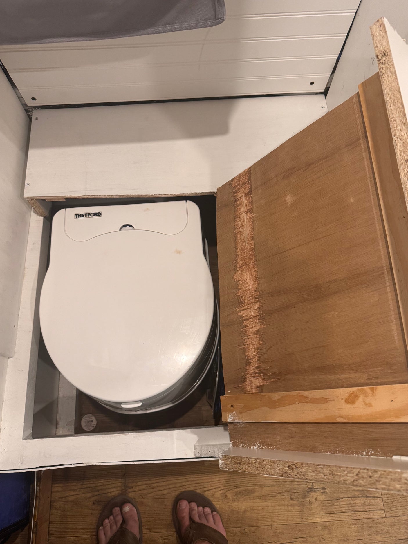 Inside an **rv rental**: a Thetford portable toilet is stored under a flip-up wooden access panel.