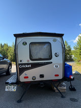 A small, light-colored Cricket travel trailer, possibly an RV rental, parked outdoors, displaying a Colorado license plate.