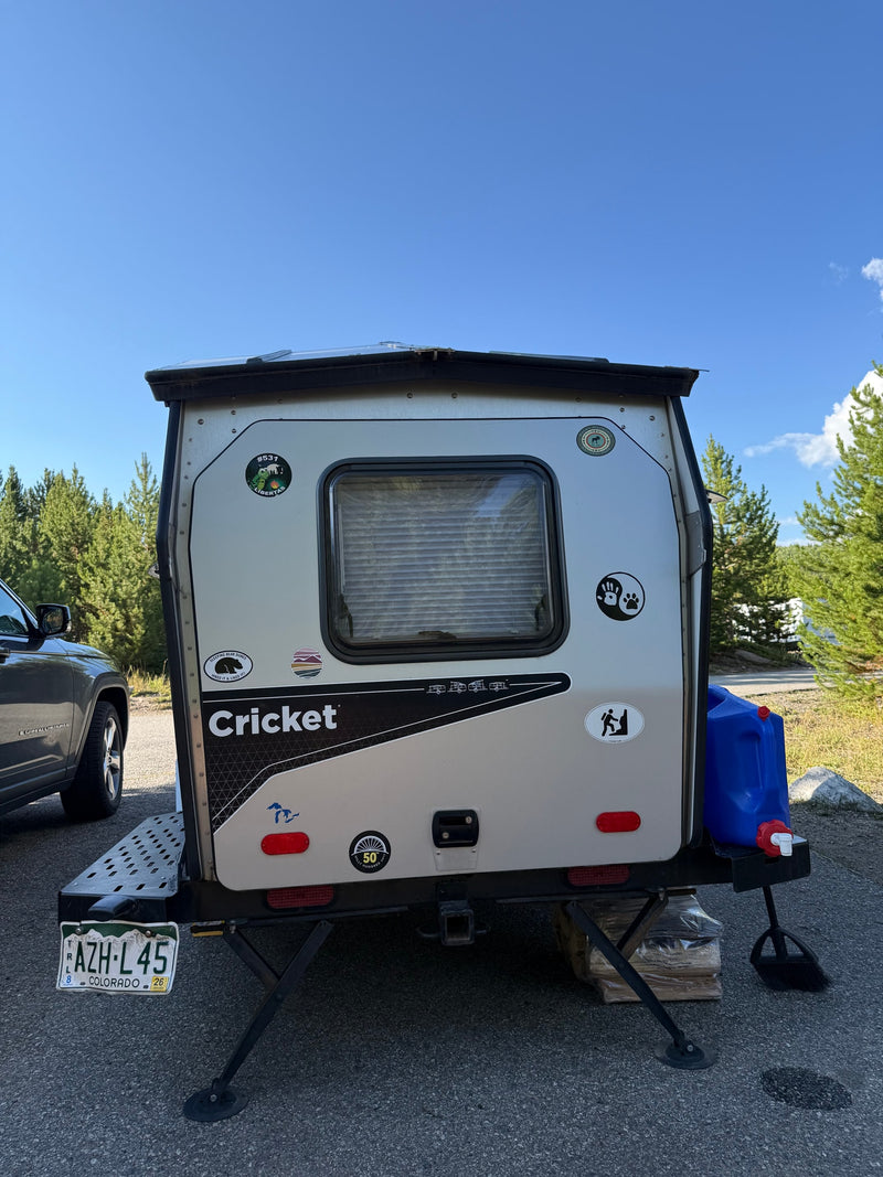 A small, light-colored Cricket travel trailer, possibly an RV rental, parked outdoors, displaying a Colorado license plate. — photo 6