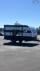 RV rental: A compact, black and white Wolf Pup travel trailer is parked outdoors on asphalt under a blue sky.