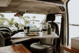 Inside an RV rental, a table is set with breakfast & coffee, overlooking a beautiful beach scene.
