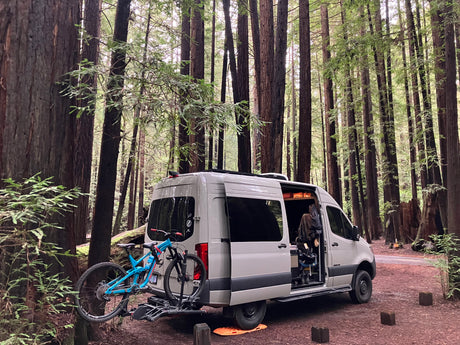RV rental van parked in a serene redwood forest with bikes, ready for outdoor adventure and exploring nature.