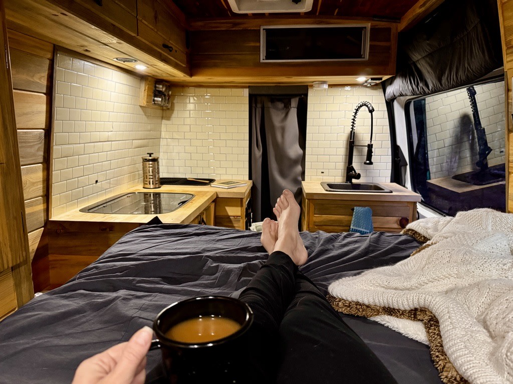  and cooktop. Efficient design for travel.|A person watches a red rock mountain sunset from their cozy **rv rental** van. Perfect view for a peaceful adventure.|Wood-paneled RV rental interior with a cozy bed — photo 7