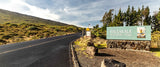 Haleakalā National Park entrance, with a sign and winding road amidst green hills. Great for an rv rental trip on Maui.
