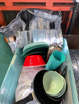 RV rental ready: a large bin packed with all kitchenware – plates, bowls, cups, a pan, and cooking utensils.