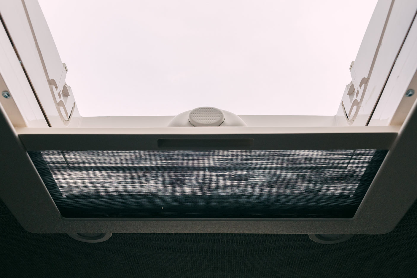 Bright RV rental interior looking up at a white roof vent. A dark mesh insect screen is pulled across.