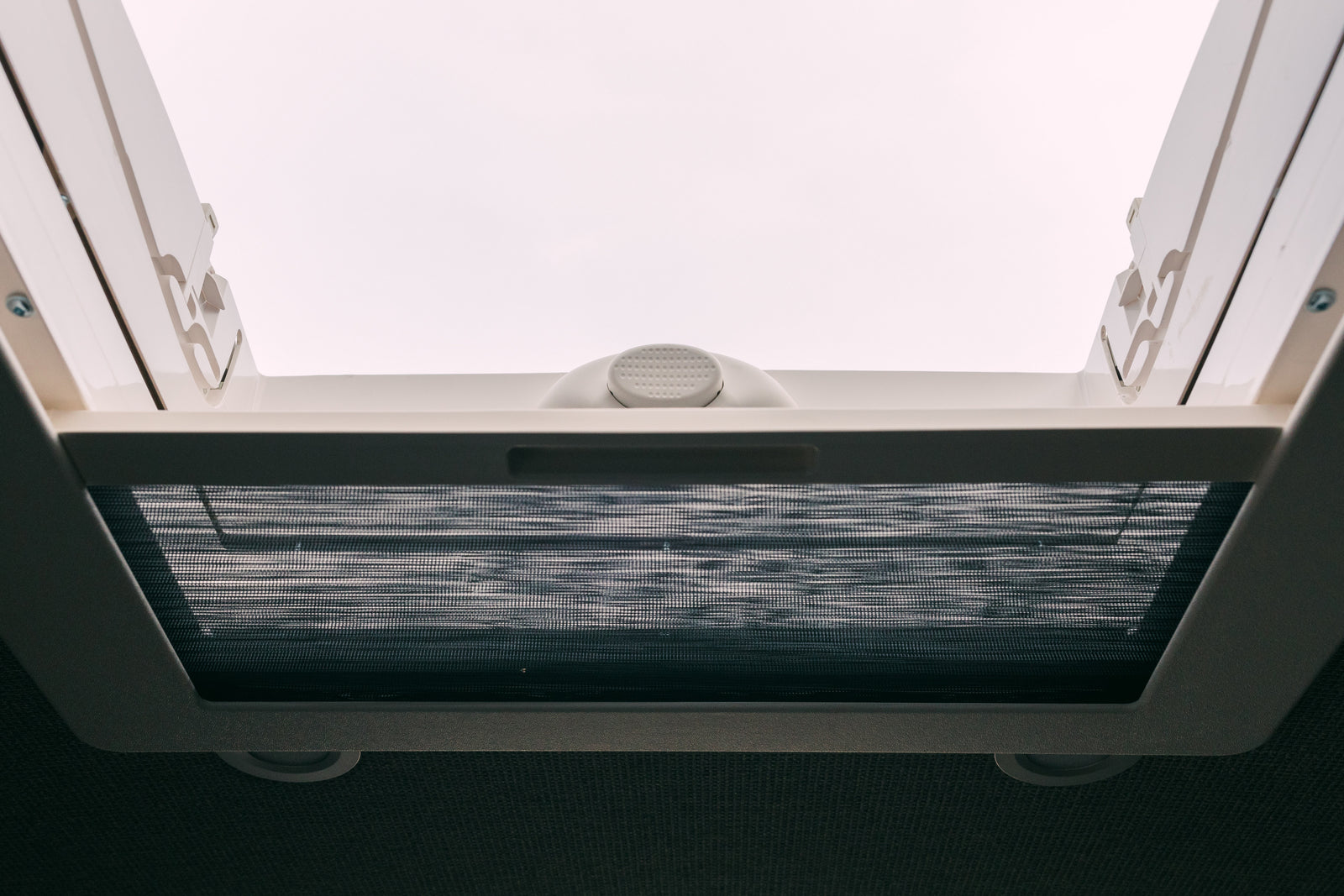 Bright RV rental interior looking up at a white roof vent. A dark mesh insect screen is pulled across.
