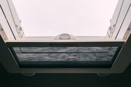 Bright RV rental interior looking up at a white roof vent. A dark mesh insect screen is pulled across.