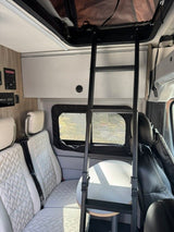 RV rental interior: Ladder to pop-top bed, quilted seats, and a table. Control panels are visible on the left wall.