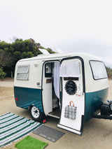 Inviting teal/white vintage camper with open door, welcome mats, & cozy interior. Perfect rv rental for camping.