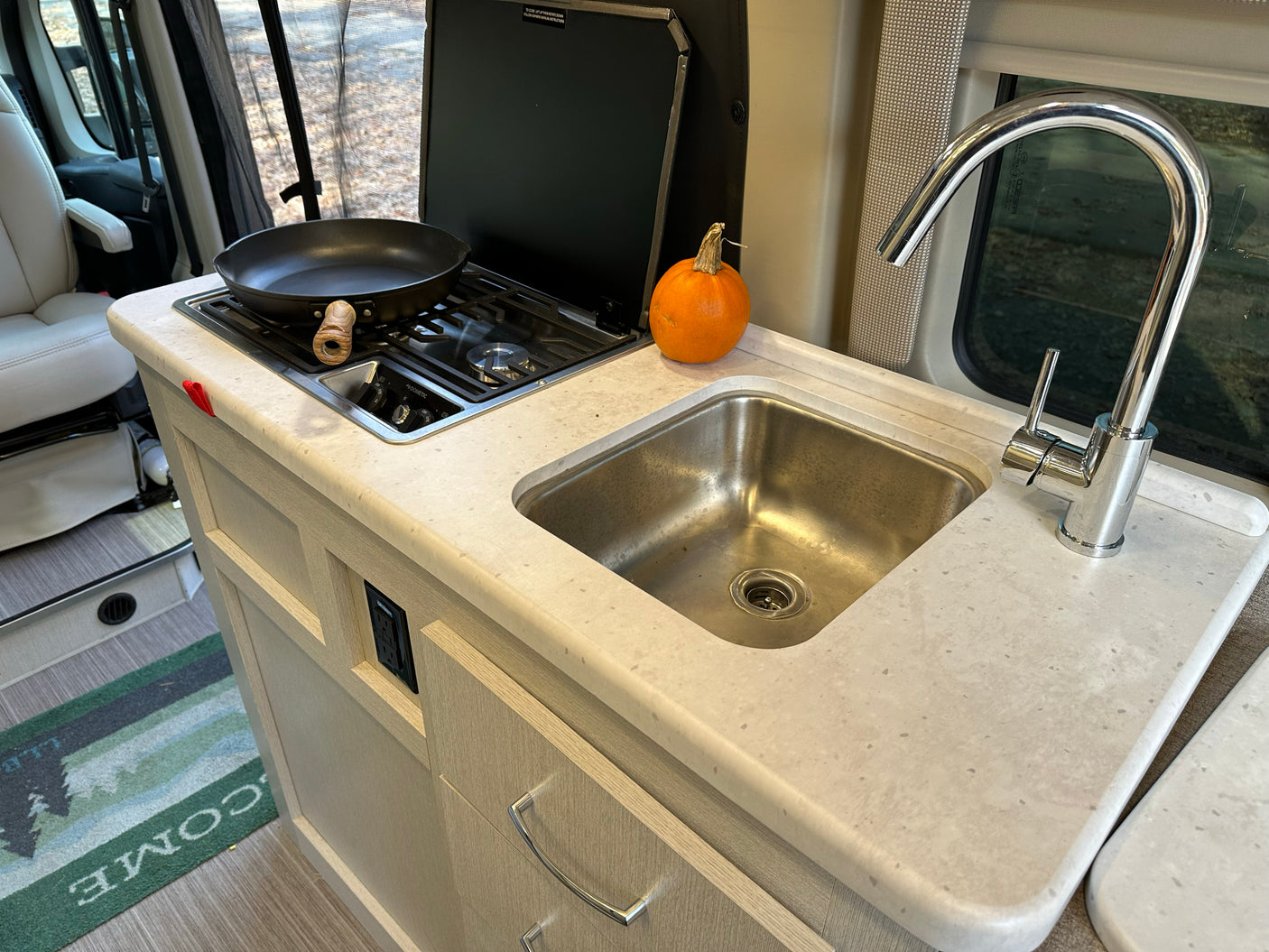Compact RV rental kitchen featuring a stovetop with pan, sink, and faucet, ideal for on-the-go cooking.