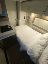 Inside an RV rental: a compact interior features a white-sheeted bed, kitchen with cooktop and fridge, plus storage cabinets.