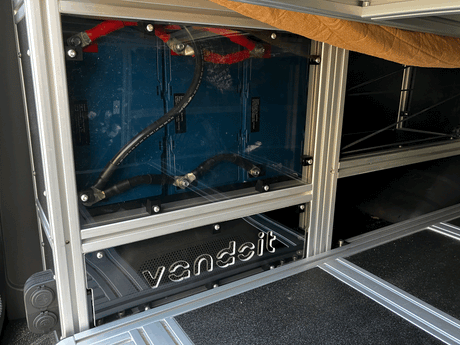 Inside an RV rental: a custom van's high-capacity lithium battery power system, visible through clear panel, with heavy-gauge cables.