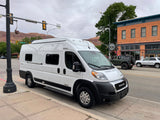 A white Winnebago Solis RV, often an RV rental, is parked on Center St. in Moab, Utah, with scenic mountains behind.