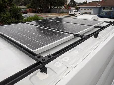 Three large solar panels on a white rv rental van's roof, mounted on a sturdy black rack. Ideal for off-grid power.