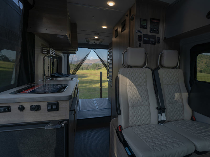 Modern RV rental interior: kitchen, comfy seating, and open back revealing a scenic view of fields and mountains. — photo 19