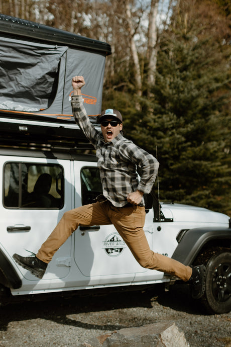 Excited man leaps by a white Jeep RV rental with a rooftop tent. Your adventure awaits with River Wild!