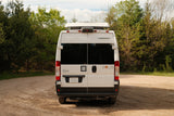Rear of a white Winnebago Solis RV rental, parked on a dirt road in a wooded setting. Ready for your next adventure.