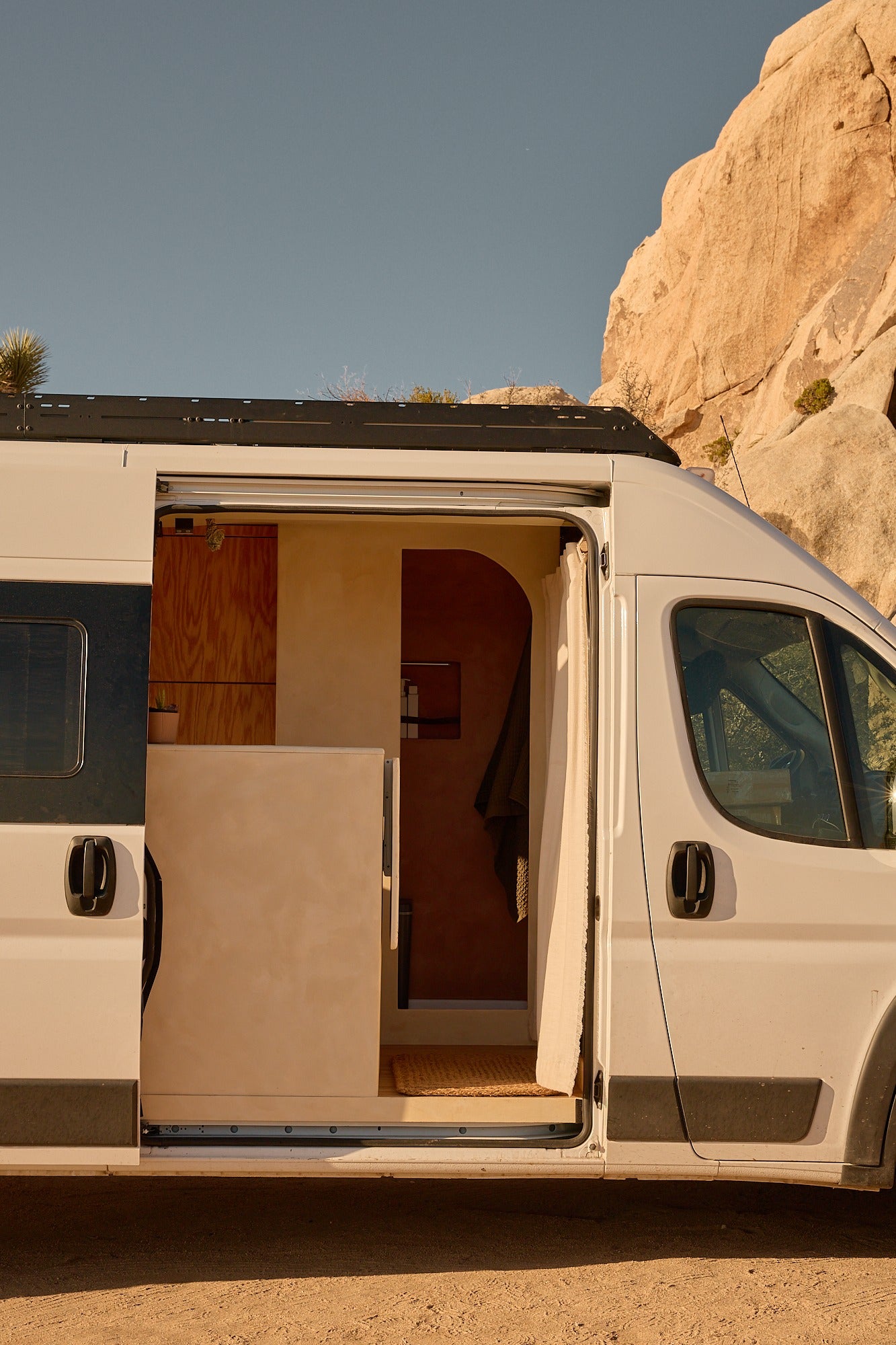 An open rv rental's custom interior, featuring wood and light-toned walls, is visible as it sits in a rocky desert landscape.