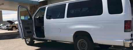 A white passenger van, with its driver's door open, appears ready for service. Perfect for group travel or your next RV rental adventure.