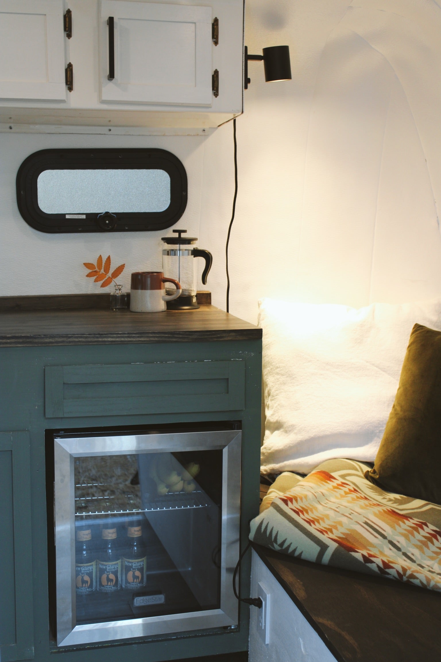 Inside a cozy RV rental: mini-fridge, coffee maker, and comfortable seating with patterned blanket and pillows.