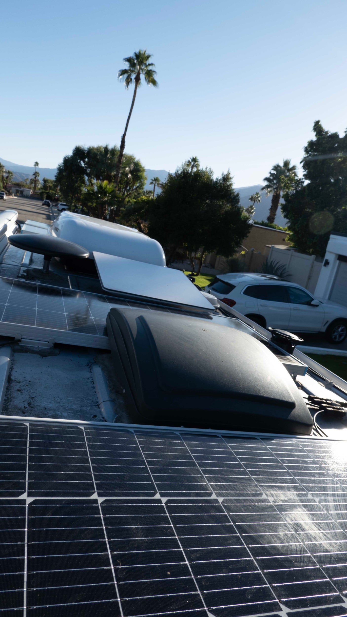 This RV rental's rooftop features solar panels, an AC unit, and a satellite dish, set against palm trees and mountains.