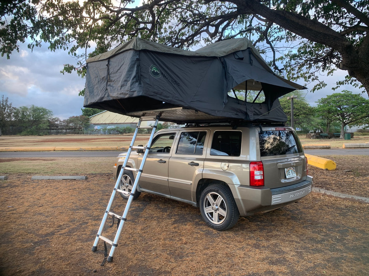 A tan Jeep Patriot with a Nomadic rooftop tent & ladder, ready for camping. Ideal for exploring, a compact rv rental option. — photo 13