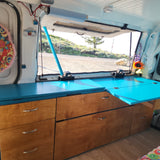 Custom camper van interior with vibrant blue counter & wooden storage, perfect for an RV rental adventure with stunning views.