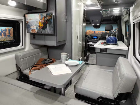 Inside a modern RV rental: a gray camper van interior with a dinette, kitchen area, and TV. Ready for your next adventure!