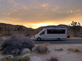 Sleek RV rental on a desert road at golden hour. See Joshua Trees and mountains. Plan your adventure road trip.