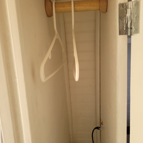 Inside an RV rental, a compact closet features a wooden hanging rod, two hangers, and wall paneling. Small yet functional.