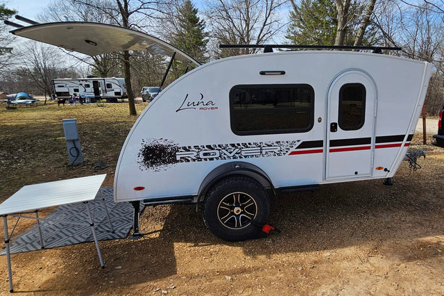  facing a calm lake and colorful sky.|A compact Luna Rover teardrop RV rental