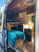 Cozy RV rental camper van interior with a bed, kitchen with sink, wooden ceiling, and flooring. Ideal for mobile living.
