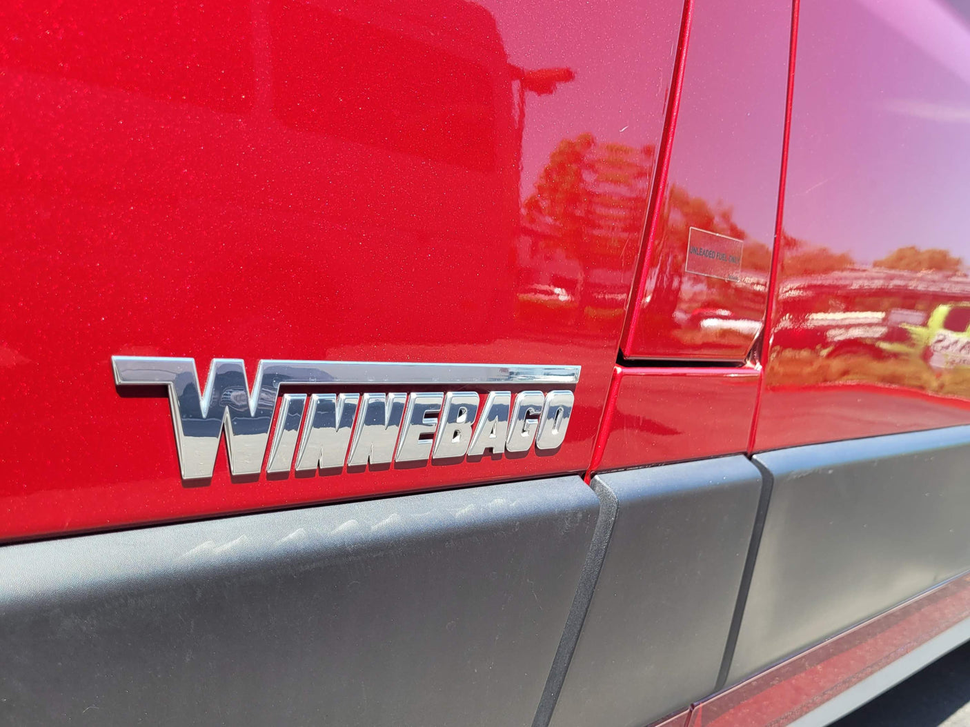 Red Winnebago RV showcasing its emblem and "UNLEADED FUEL ONLY" sticker, ready for your next rv rental.