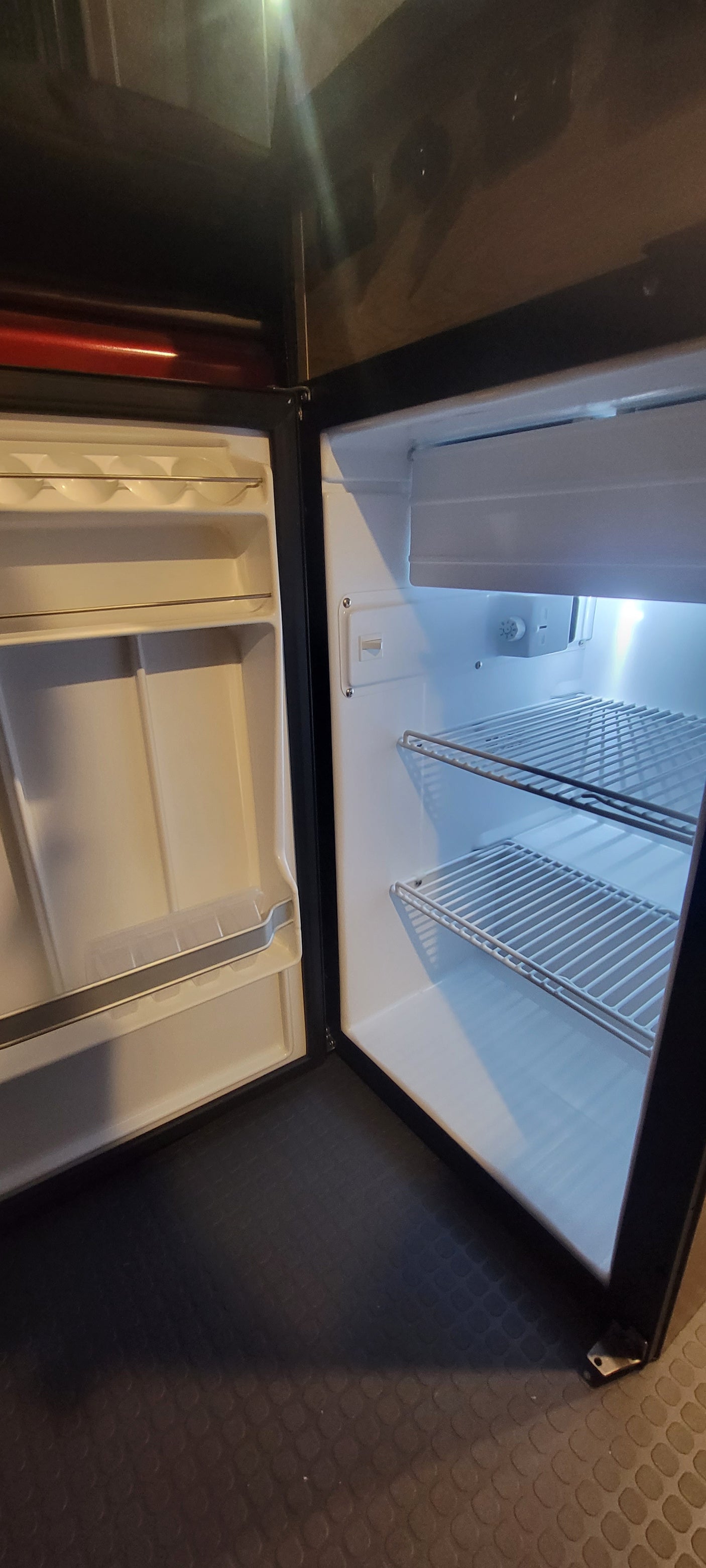 Clean RV rental refrigerator and freezer interior, featuring shelving and a temperature control dial, ready for your journey.