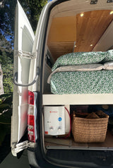 Cozy RV rental interior shows a bed, Camplux water heater, and storage, perfect for van life adventures.