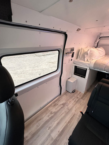 Inside an rv rental: a modern campervan conversion with bed, window, light wood floor, and rear seats.